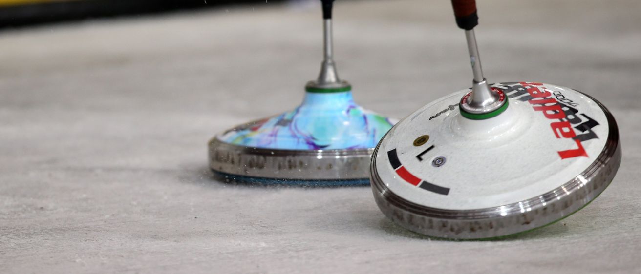 Zwei Dartspinner, einer mit einem blauen und grünen Griff und der andere mit einem braunen Griff, drehen sich auf einer grauen Oberfläche.