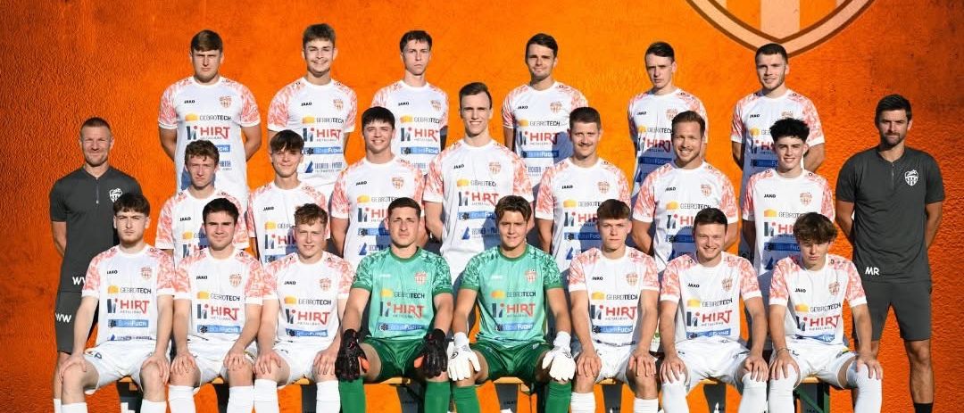 Ein Teamfoto der Fußballmannschaft für die Saison 2025/26, die Spieler vor dem Teamlogo. Das Logo zeigt einen Fußball, Sterne und den Text 'Wir sind Greinerbach'. Die Spieler tragen Trikots mit verschiedenen Sponsorenlogos.