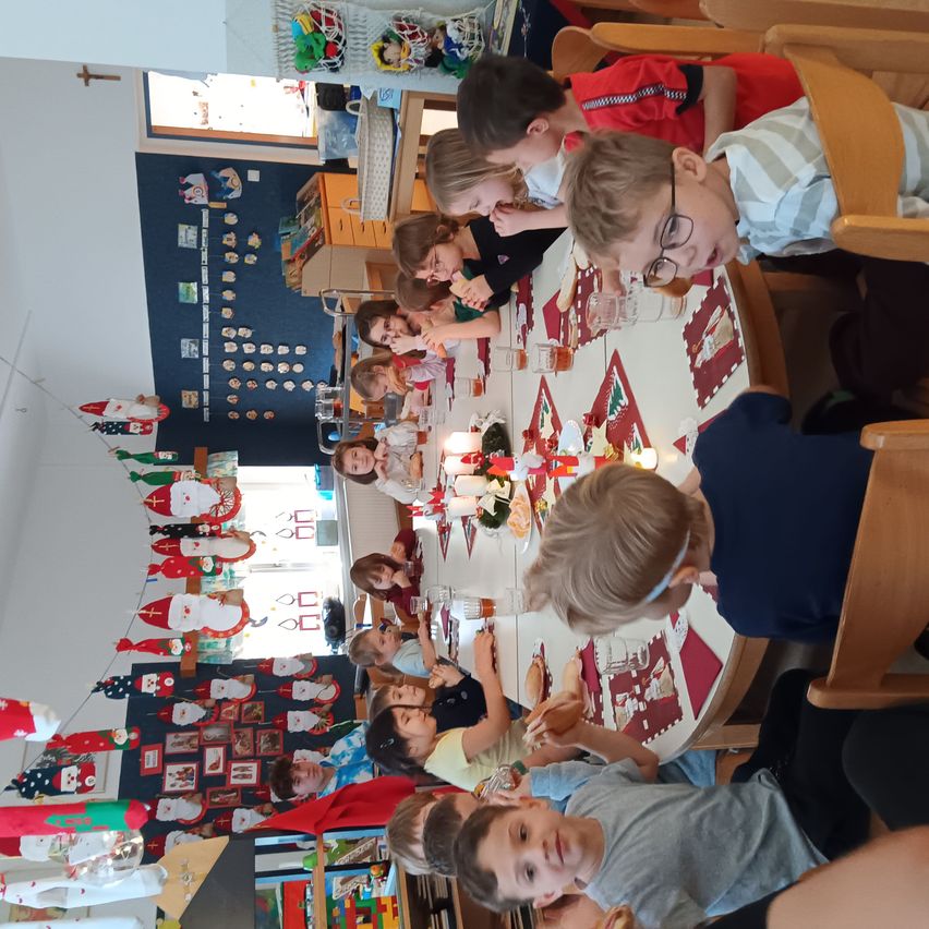 Eine Gruppe von Kindern sitzt an einem festlich gedeckten Tisch und genießt das Essen. Der Tisch ist mit weihnachtlichen Themen geschmückt, und sie sind von Feiertagsdekorationen umgeben.