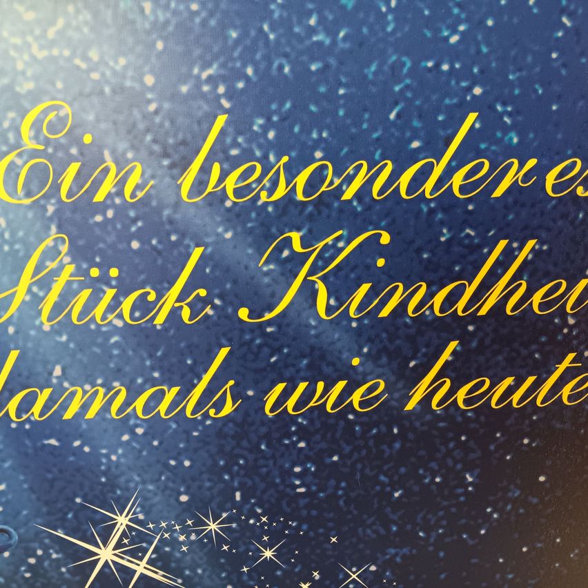 Ein blauer Hintergrund mit gelbem Text, der 'Ein besonderes Stück Kindheit damals wie heute' lautet. Der Text ist von einem Muster weißer Sterne umgeben.