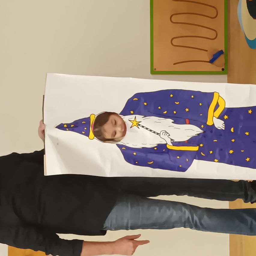 Ein Kind, das als Zauberer verkleidet ist, hält ein Banner mit einem Zaubererbild, während eine Person hinter ihm in einem Raum steht.