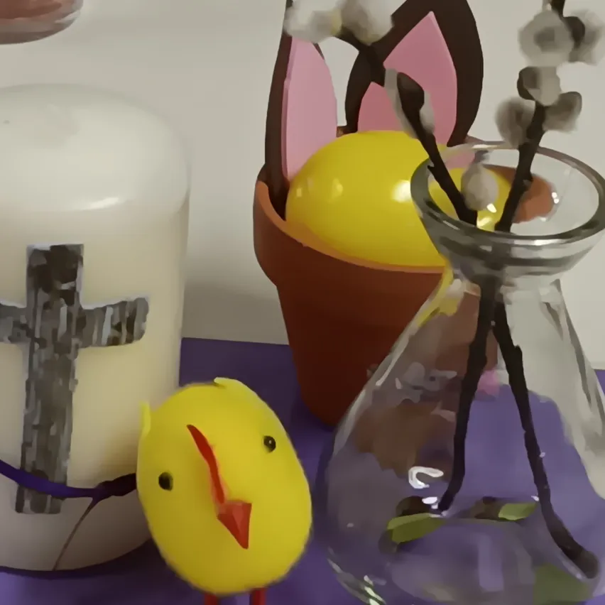 Eine weiße Kerze mit einem Kreuz und einem gelben Osterhähnchen auf einer violetten Oberfläche. Eine Vase mit Ostereiern und Weidenzweigen.