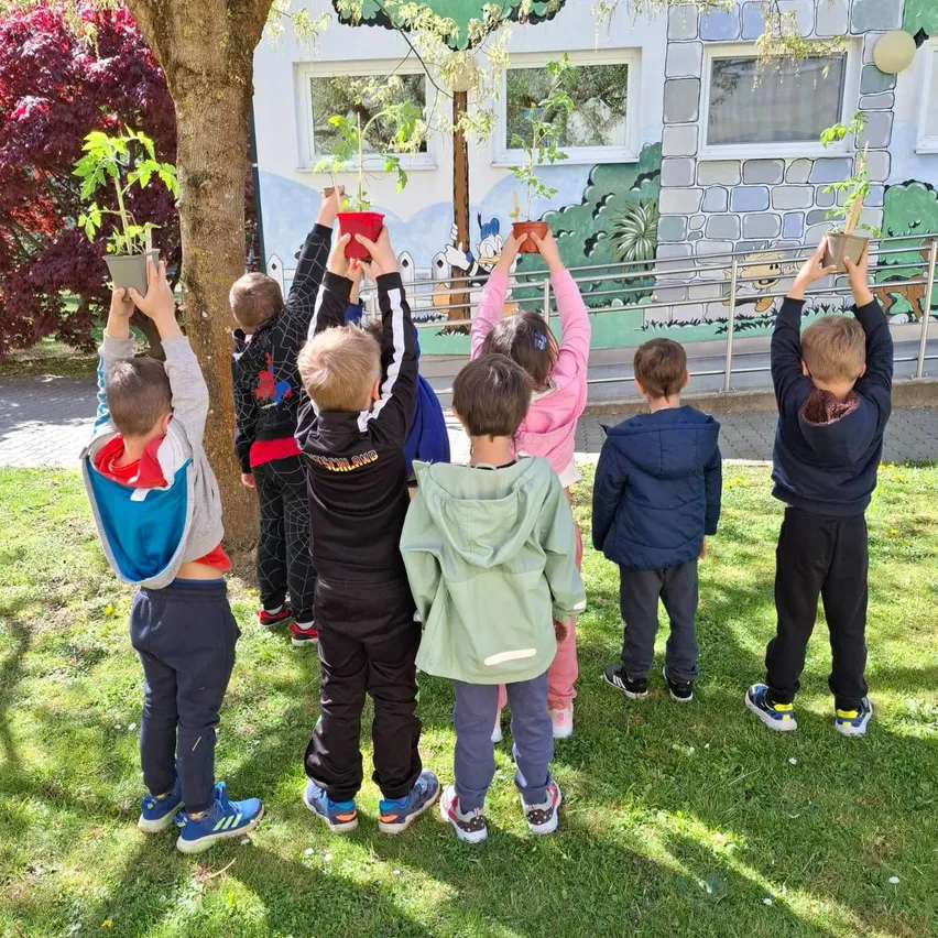 Kinder halten kleine Topfpflanzen, möglicherweise zum Pflanzen, an einem sonnigen Tag vor einer Wandmalerei.