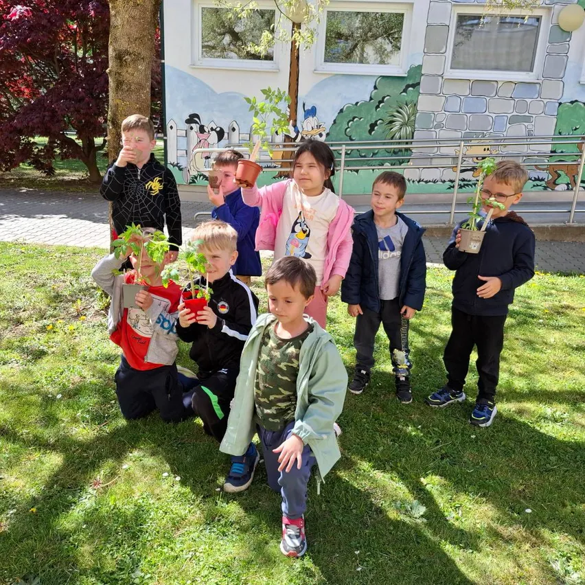 Mehrere Kinder posieren für ein Foto mit Topfpflanzen vor einem Gebäude mit bunten Wandgemälden.