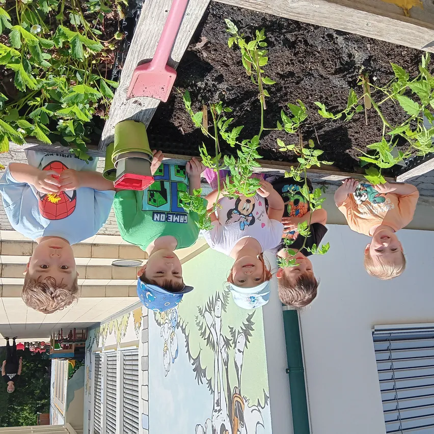 Fünf Kinder sind in einem Garten. Sie schauen nach oben und lächeln. Sie tragen Mützen und Shirts mit Bilder von Charakteren.