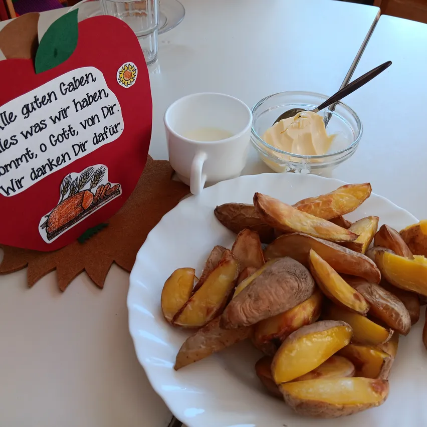 Ein Teller mit gebratenen Kartoffeln, eine Tasse Milch und eine Schüssel Butter auf einem weißen Tisch.