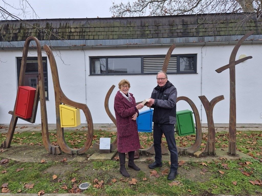 An elderly woman and a man are standing in front of a building with colorful boxes, possibly exchanging something.
