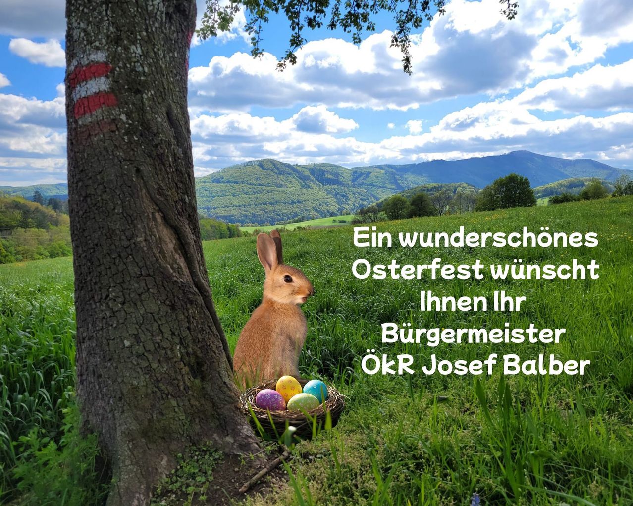 A rabbit is sitting next to a tree with colorful Easter eggs in a basket. A message in German reads 'A wonderful Easter festival' and is signed by Mayor Josef Balbe.