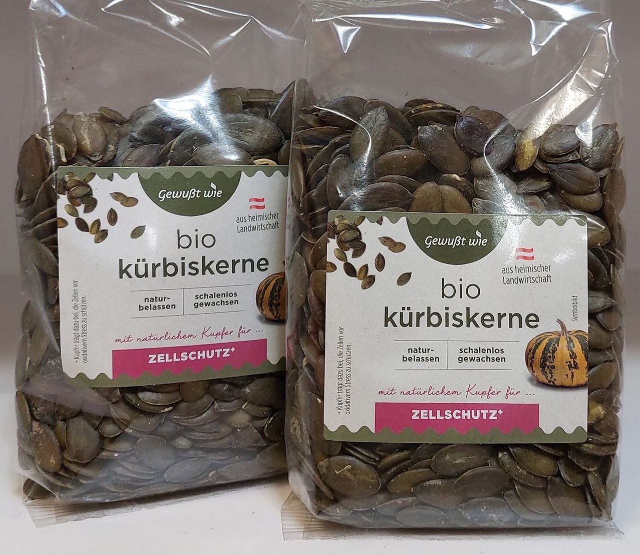 Zwei Plastiktüten mit Bio-Kürbiskernen. Sie sind ungeschält, schalelos und natürlich angebaut. Das Etikett zeigt eine Illustration von Kürbis und Text auf Deutsch.
