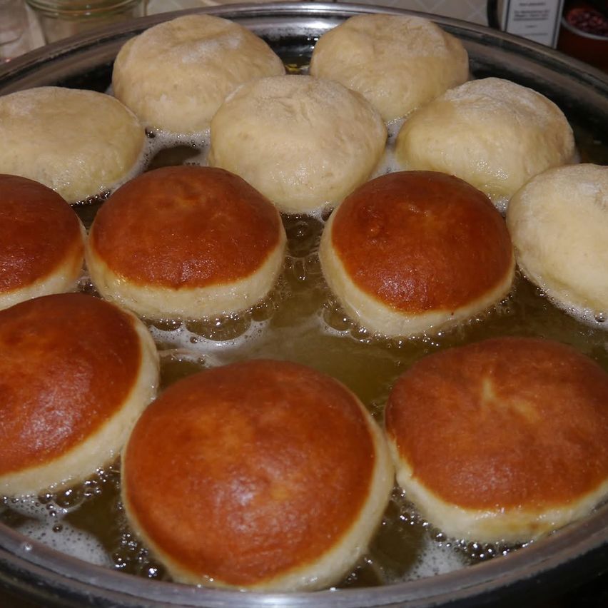 Eine Metallschüssel mit Teigbällen, die in kochendem Öl garen, einige goldbraun, andere noch blass.