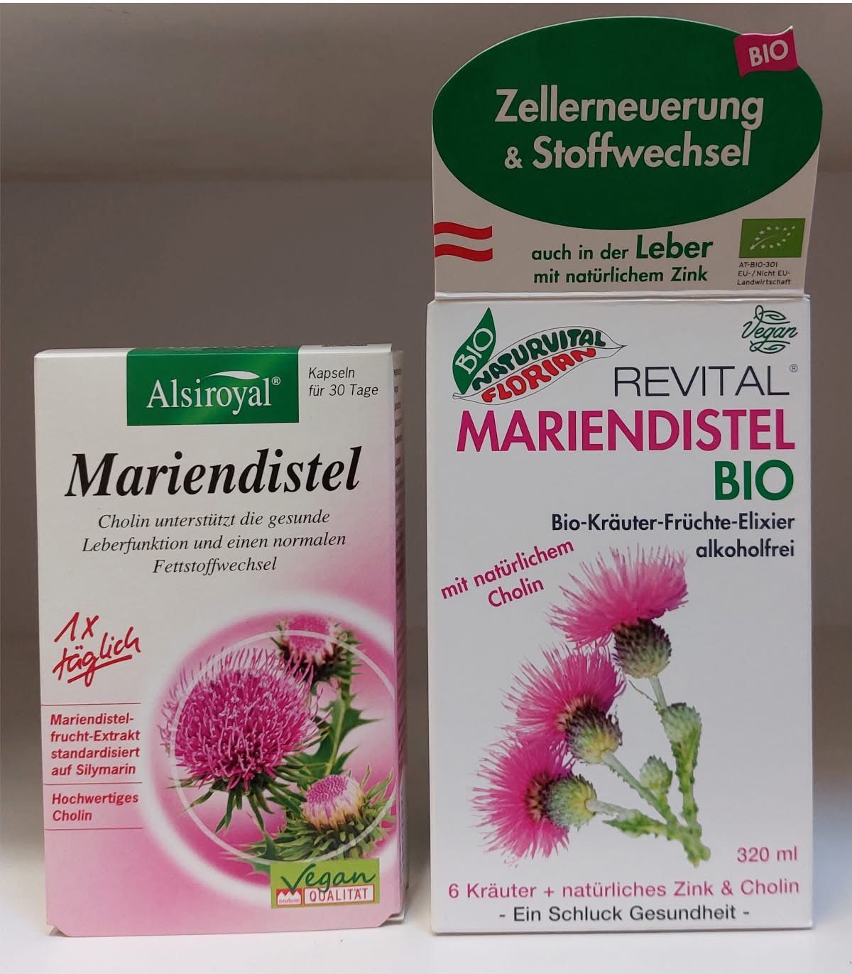 Zwei Gesundheitsproduktverpackungen sind zu sehen. Die erste Schachtel, mit 'Mariendistel' von Alsiroyal beschriftet, enthält 30 Kapseln. Die zweite Schachtel, mit 'Revital Mariendistel BIO' beschriftet, enthält 320 ml eines Kräuterextrakts. Beide Produkte zeigen die Goldrute und behaupten, die Lebergesundheit zu unterstützen.