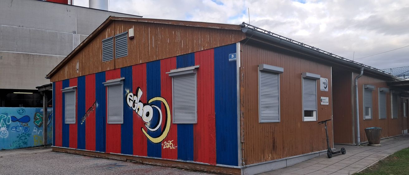 Ein kleines Gebäude mit roten und blauen Streifen und dem Wort Echo darauf. Vor ihm steht ein Roller geparkt.