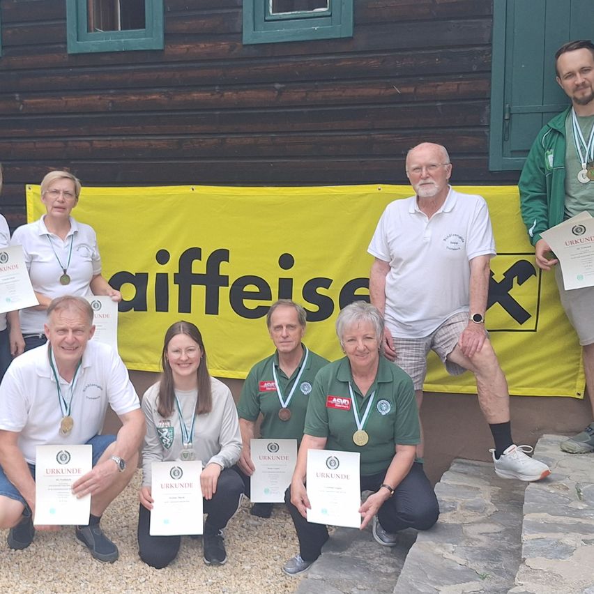 Eine Gruppe von Menschen in grünen und weißen Uniformen posiert für ein Foto mit Zertifikaten vor einem Holzgebäude mit einem gelben Banner.