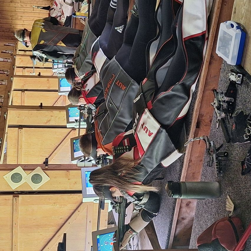 Eine Gruppe von Menschen nimmt an einem Schießwettbewerb teil, trägt Schutzausrüstung und zielt auf Ziele an einer Wand.