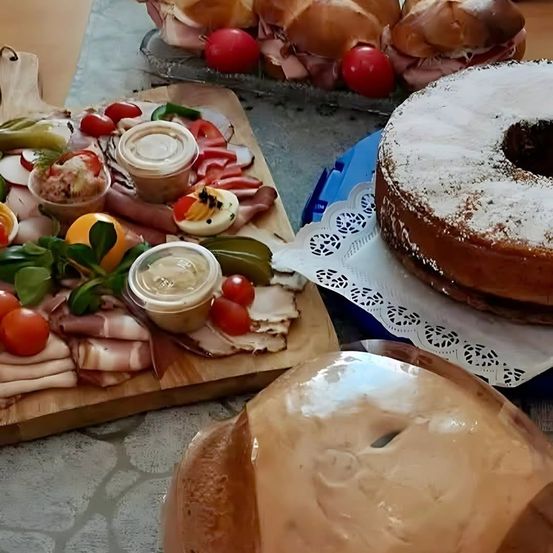 Ein Tisch mit einem Charcuterie-Brett mit Fleisch, Käse, Gewürzgurken und einem pulverisierten Kuchen.