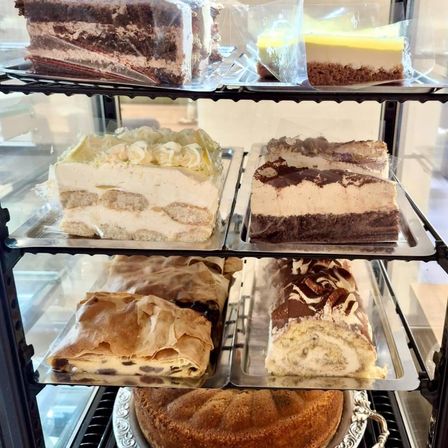 Eine Vitrine mit verschiedenen Desserts, darunter Schichtkuchen, Käsekuchen und ein Schokoladenrollenkuchen, alle ordentlich auf Tabletts angeordnet.