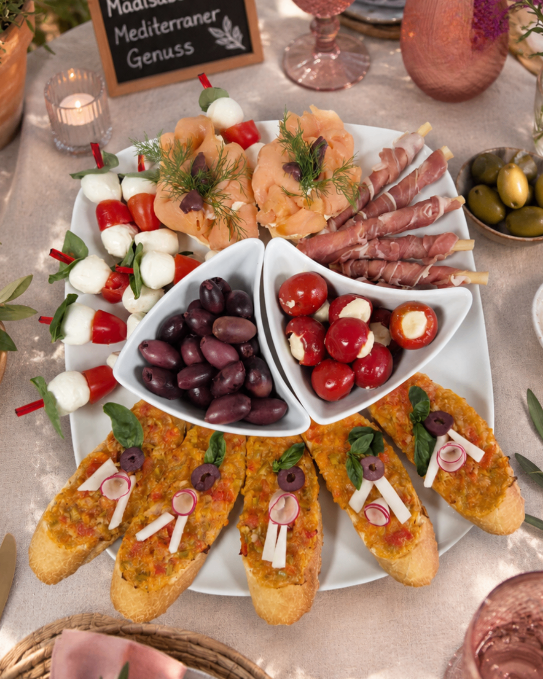 A white platter with various appetizers, including olives, cherry tomatoes, cheese, and bread with toppings.