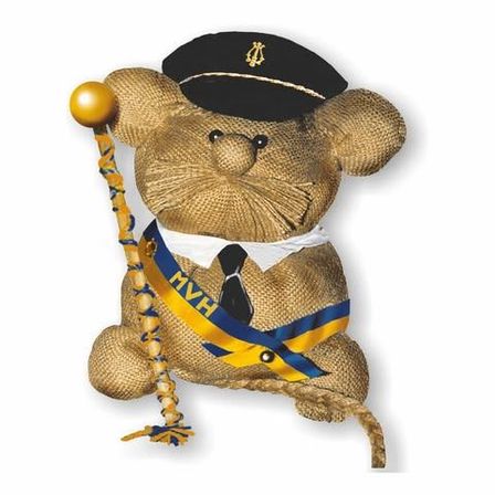 Ein Stoffteddybär verkleidet als Kapitän, trägt einen schwarzen Hut, blau-gelbe Schärpe und hält einen goldbesetzten Gehstock.