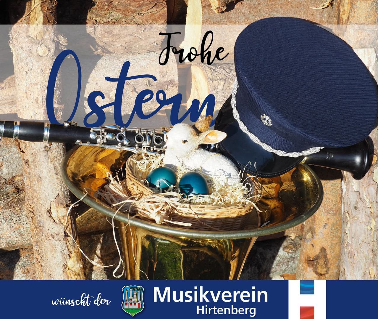 Eine Trompete und eine Flöte liegen auf einem Baumstumpf. Ein Schaf ruht in einem Nest mit blauen Eiern, und ein blauer Hut liegt in der Nähe. Der Text lautet 'Frohe Ostern'. Logo für Musikverein Hirtenberg unten.