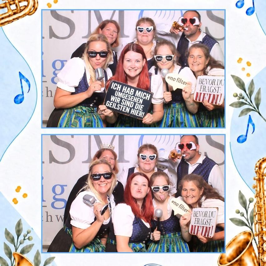 A group of people dressed in traditional German attire, holding microphones and signs, posing for a photo booth picture. The signs read 'Ich hab mich umgesehen wir sind die geilsten hier!' and 'Bevor du fragst nein!'. The background features musical notes and saxophones.