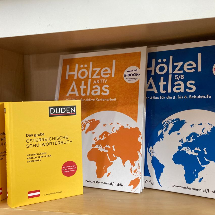 Ein Regal hat vier Bücher. Drei davon sind Atlanten und eines ist ein Wörterbuch. Die Atlanten sind betitelt Holzel Atlas und Holzel Atlas 5/8. Das Wörterbuch ist betitelt Das große österreichische Schulwörterbuch.