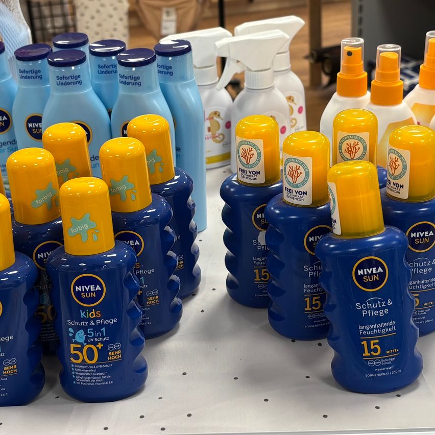 Eine Anzeige von blauen und gelben Flaschen der Nivea Sun Sonnencreme mit verschiedenen LSF-Werten, einschließlich Kids 50+ und 15, auf einem weißen Regal angeordnet.