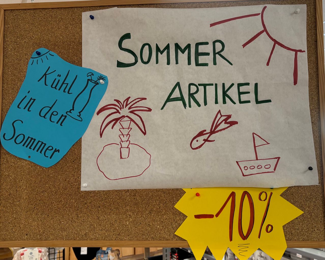 Ein Anschlagbrett zeigt ein weißes Papier mit grünem Text, der 'SOMMER ARTIKEL' lautet. Das Papier hat Zeichnungen einer Palme, eines Fisches und einer Sonne. Ein blaues Papier mit dem Text 'Kühl den sommer' ist links angeheftet. Ein gelbes Papier mit dem Text '-10%' ist unten angeheftet.
