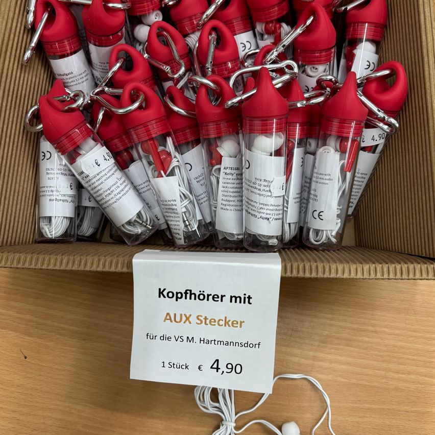 A box of red plastic cases with earphones inside, each case has a red cap and a white label with text. A white sign on the box reads Kopfhörer mit AUX Stecker.