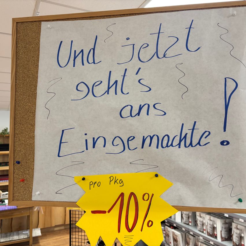 A bulletin board with a handwritten note in blue reads 'And now it sees's ans P Einge macht'. A yellow tag with '-10%' is pinned below.