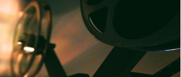 Eine Nahaufnahme eines alten Filmprojektors mit einem hellen Licht vorne, das die Filmrolle darüber beleuchtet.