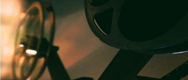 Ein Filmprojektor zeigt eine Nahaufnahme des Filmtons und der Lampe. Die Lampe ist eingeschaltet und wirft ein helles Licht auf die Umgebung.