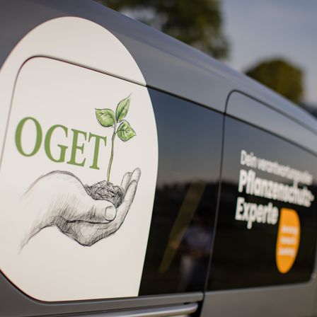 Die Seite eines Fahrzeugs zeigt das Logo von OGET mit einer Hand, die eine aus Erde sprießende Pflanze hält. Der Text lautet 'Pflanzenschutz-Experte'.