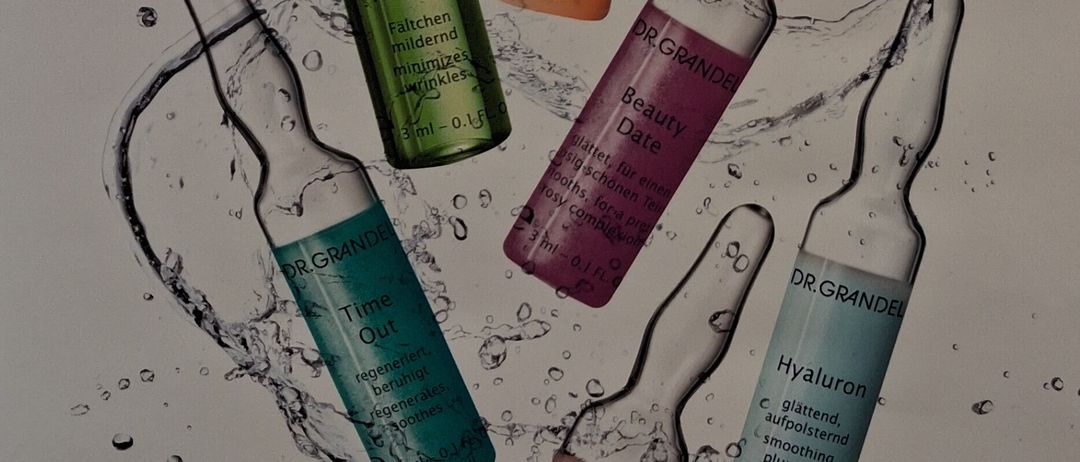 Werbeplakat für Dr. Grandel Produkte mit sechs illustrierten Ampullen mit den Bezeichnungen Beauty Flash, Retinol, Time Out und Hyaluron. Wasserspritzer umgeben die Flaschen. Das Plakat trägt den Titel Einladung zur Dr. Grandel Beratung.