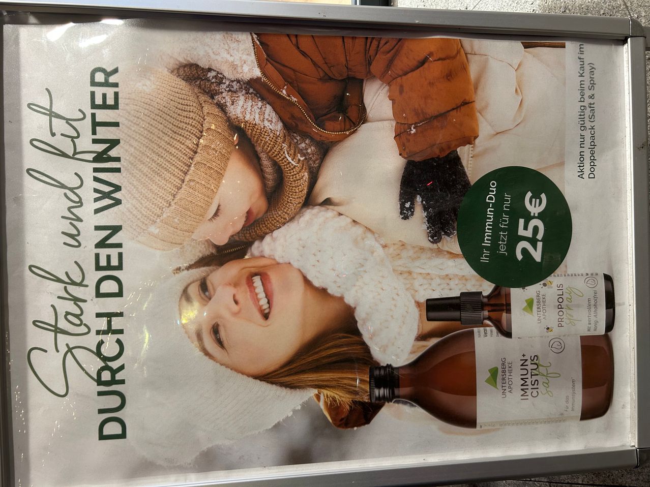 Ein Poster zeigt eine Frau und ein Kind, die in Winterkleidung eingepackt sind. Das Poster bewirbt ein Produkt namens 'Immun-Cistus' mit einem Preisschild von 25 Euro.