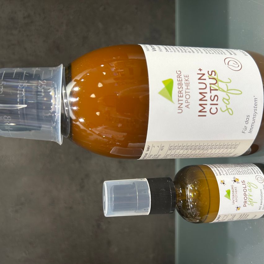 Zwei Flaschen, eine mit der Aufschrift 'Immune+ Cistus' und die andere 'Propolis', beide scheinen pflanzliche Heilmittel zu sein, auf einer reflektierenden Oberfläche platziert.