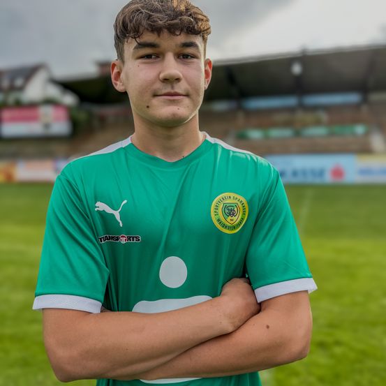 Ein Fußballspieler in einem grünen Trikot mit einem weißen Puma-Logo auf der Brust steht auf einem grünen Feld.