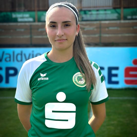 Eine Frau in einem grünen und weißen Fußballtrikot mit der Nummer 9 posiert für ein Foto auf dem Feld.