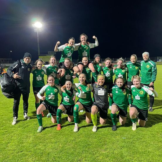 Eine Fußballmannschaft in grünen Trikots posiert für ein Foto auf einem Feld bei Nacht, mit zwei Spielern auf anderen.