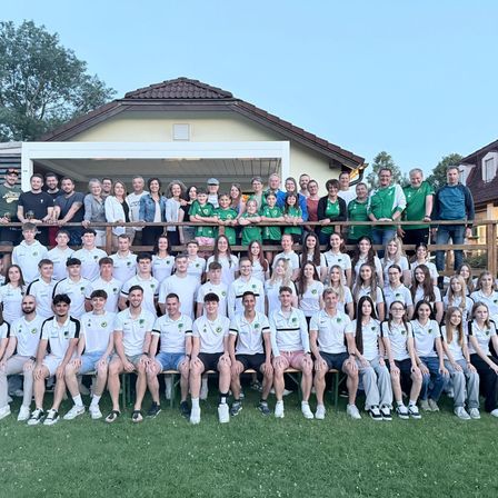 Eine Gruppe von Personen in grünen und weißen Uniformen posiert für ein Foto auf einem Rasen vor einem Haus.
