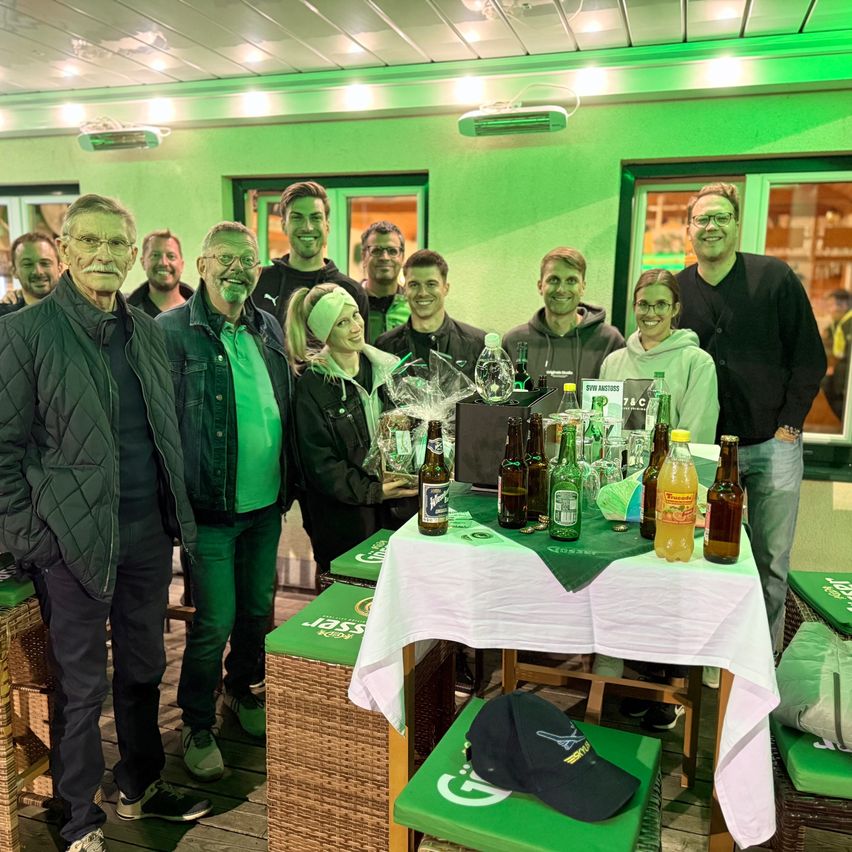 Eine Gruppe von Menschen in Grün posiert für ein Foto in einem Restaurant mit einem Tisch, der mit Flaschen bedeckt ist, und einer Kappe auf einem Hocker.