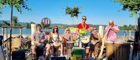 Eine Gruppe von Menschen steht mit Musikinstrumenten auf einer Bühne, möglicherweise bei einer Aufführung. Die Bühne ist im Freien.