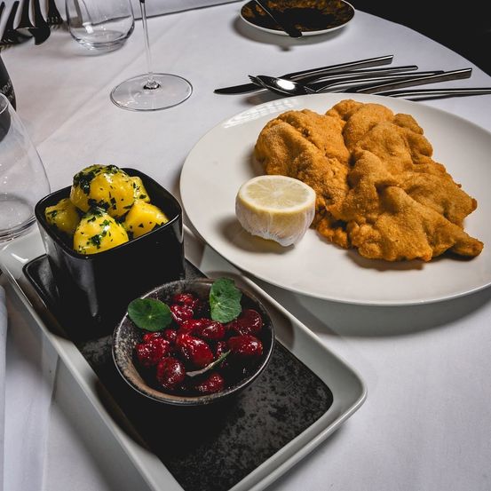 Ein Tisch für eine Mahlzeit mit einem Teller mit gebratenen Kartoffeln, einer Schüssel mit gelben Kartoffeln und einer Schüssel mit roten Kirschen.