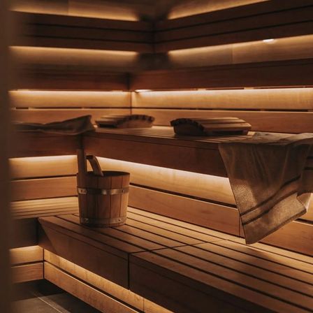 Eine hölzerne Sauna mit einem Eimer und Handtüchern auf den Bänken, beleuchtet von warmem Licht.