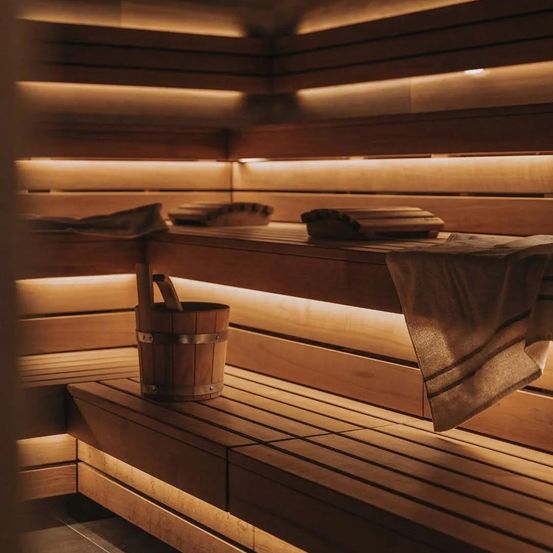 Eine hölzerne Sauna mit einem Eimer und Handtüchern auf den Bänken, beleuchtet von warmem Licht.