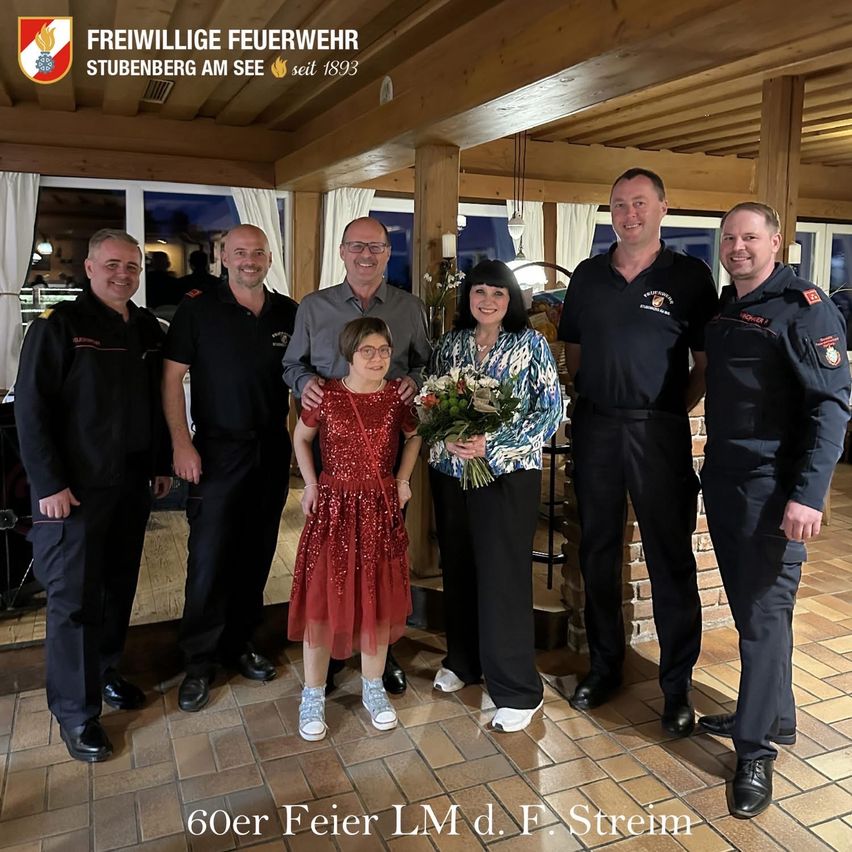 Freiwillige Feuerwehrleute in Uniform feiern ein 60-jähriges Jubiläum. Ein Mädchen in einem roten Kleid erhält einen Blumenstrauß.
