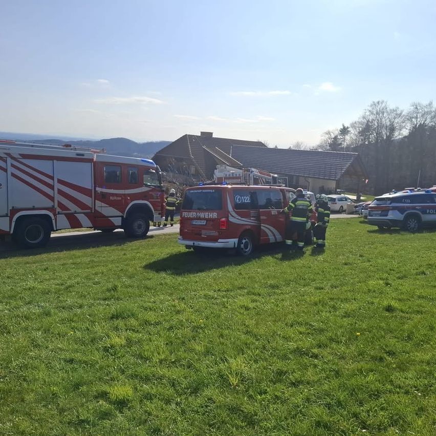 Feuerwehrfahrzeuge und Polizeiwagen sind auf einem Rasenfeld in der Nähe eines Hauses geparkt. Feuerwehrleute und Polizisten stehen neben den Fahrzeugen.