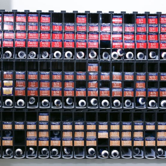 Eine Sammlung verschiedener farbiger Etiketten mit Zahlen und Zeiten, die in einem Rasterformat auf einem weißen Hintergrund angeordnet sind. Die Etiketten enthalten Zahlen wie 44/65, 55/46 und Zeiten wie 7/00, 8/00, 9/00 usw.