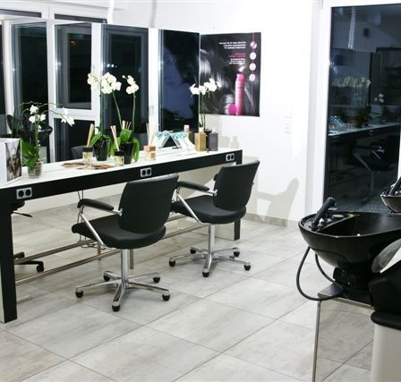 Ein Salonbereich mit Schreibtisch, Stühlen und Waschbecken. Der Schreibtisch hat Blumen und Flaschen. Die Stühle sind schwarz. Das Waschbecken ist schwarz.