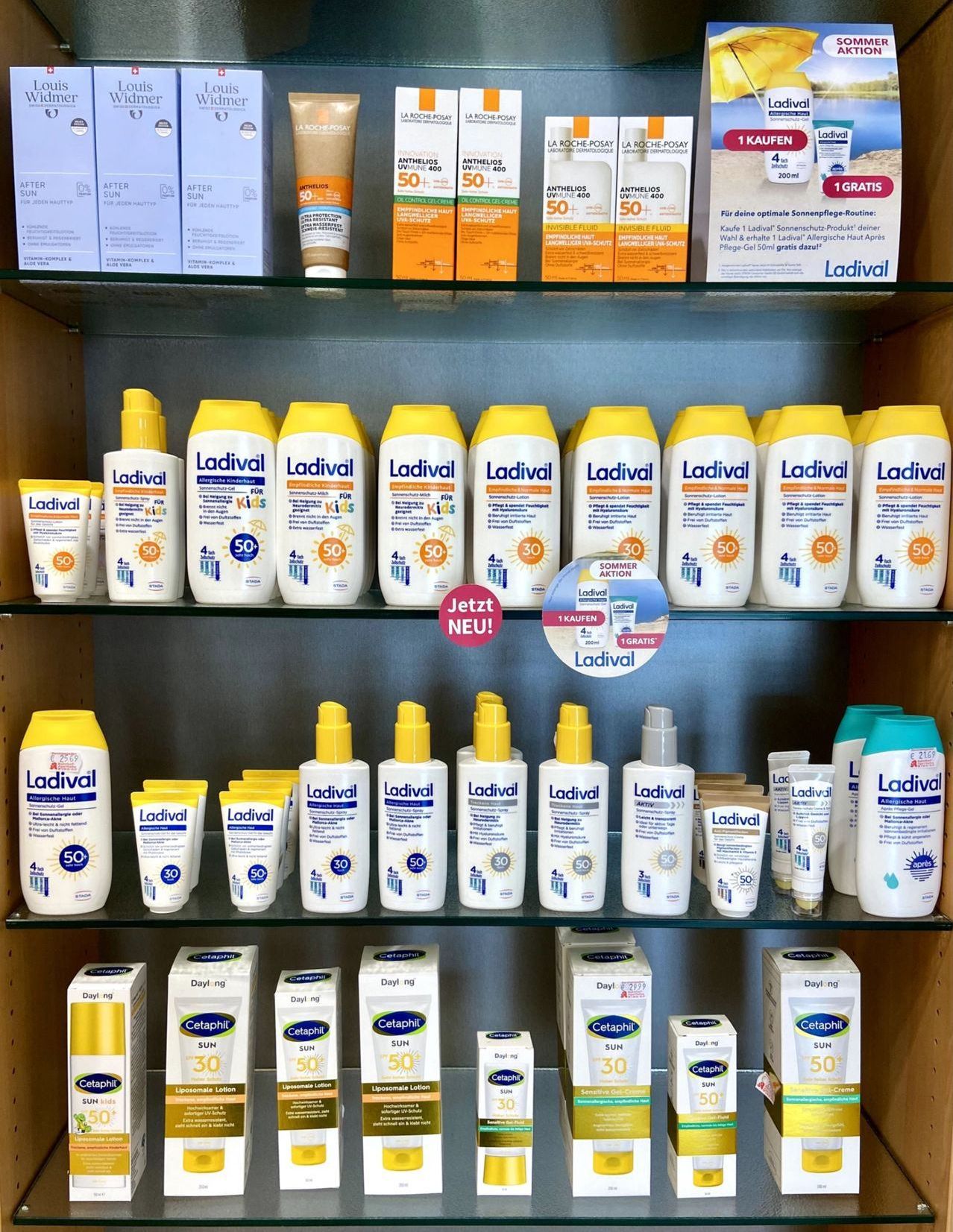 A pharmacy shelf displays various sunscreen products, including Ladival sunscreen bottles and Cetapihl sunscreen boxes, all labeled with SPF values and some marked as 'Jetzt NEU!' and 'GRATIS'.