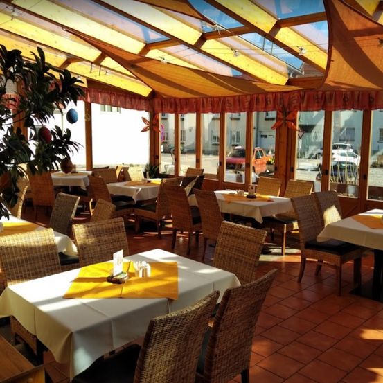 Ein Restaurant mit weißen Tischdecken und Korbstühlen. Das Innere hat ein gelbes Dach. Es sind mehrere Autos draußen geparkt.